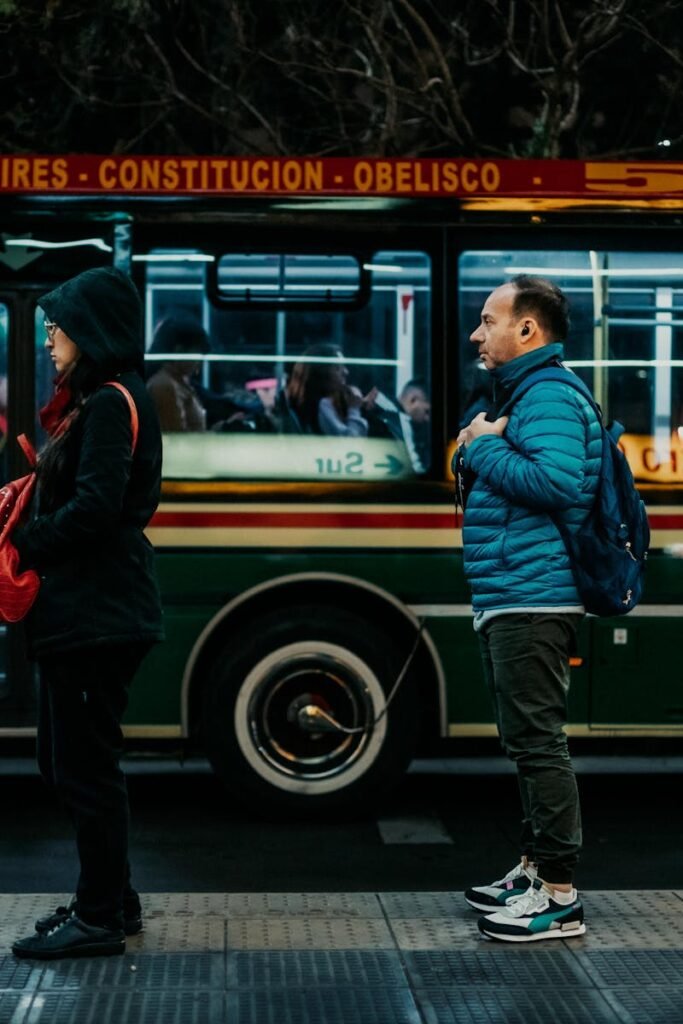 Commuters line up at night in Buenos Aires, waiting beside a colorful city bus.